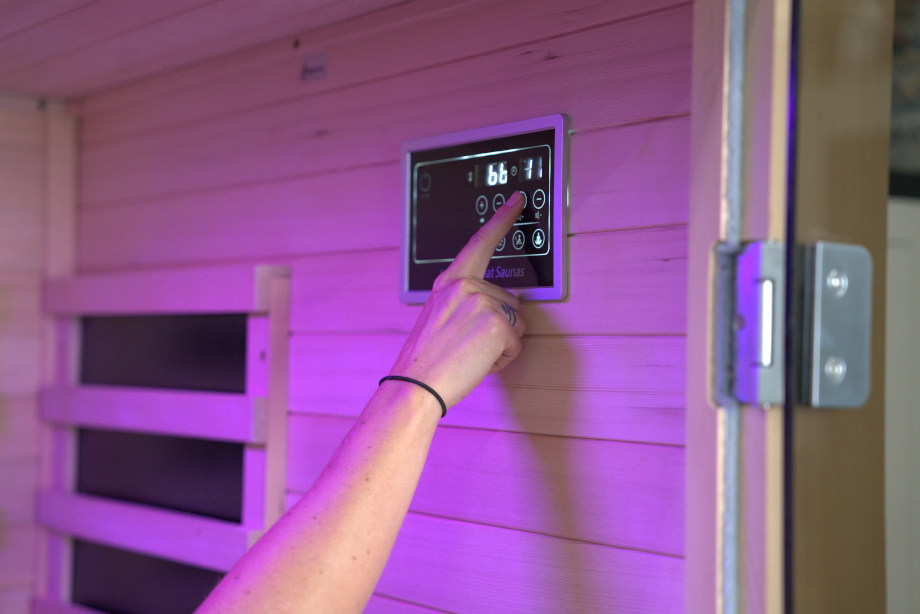 A hand interacts with the control panel on a Heavenly Heat 2-Person Sauna