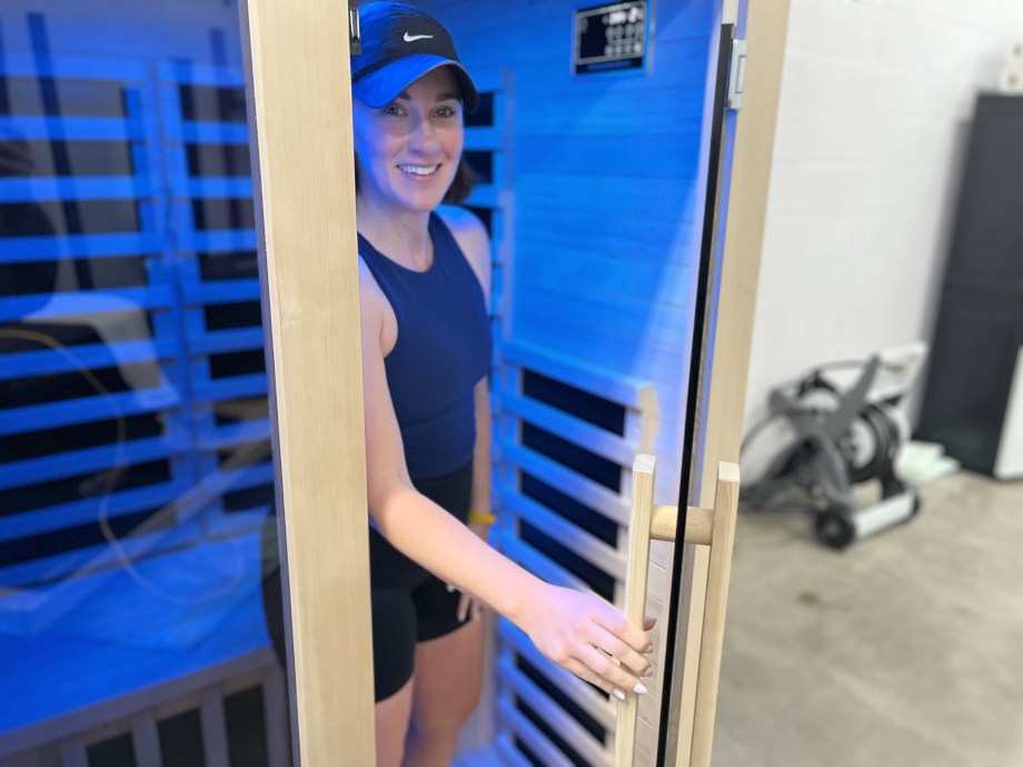 A woman smiles from inside the door of a Heavenly Heat 1-Person Sauna