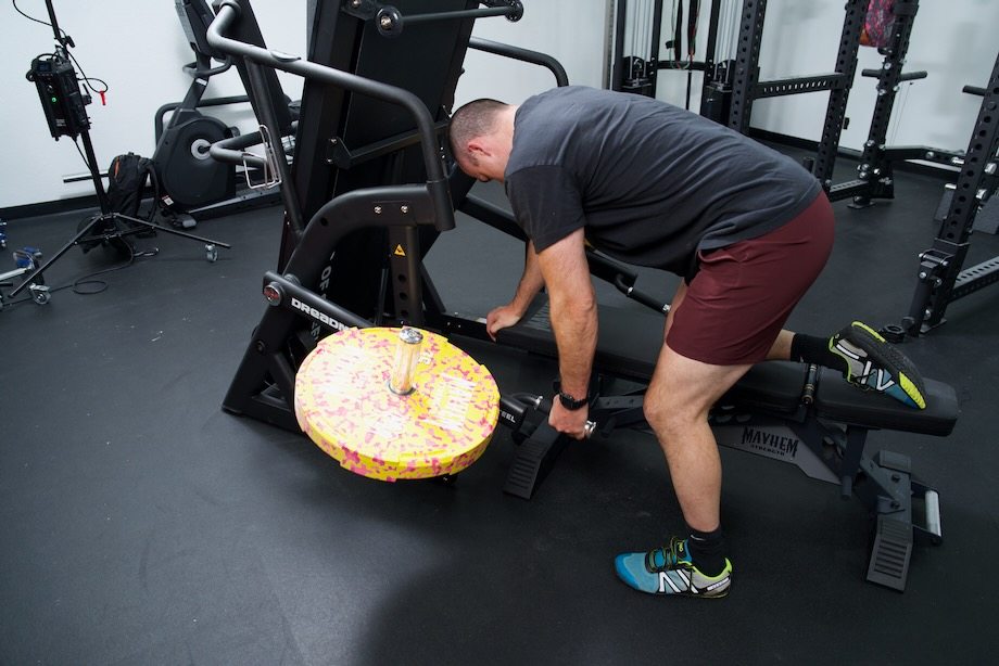 Coop leans a knee on the bench of a Bells of Steel Dreadmill and lifts one of the weight plates.