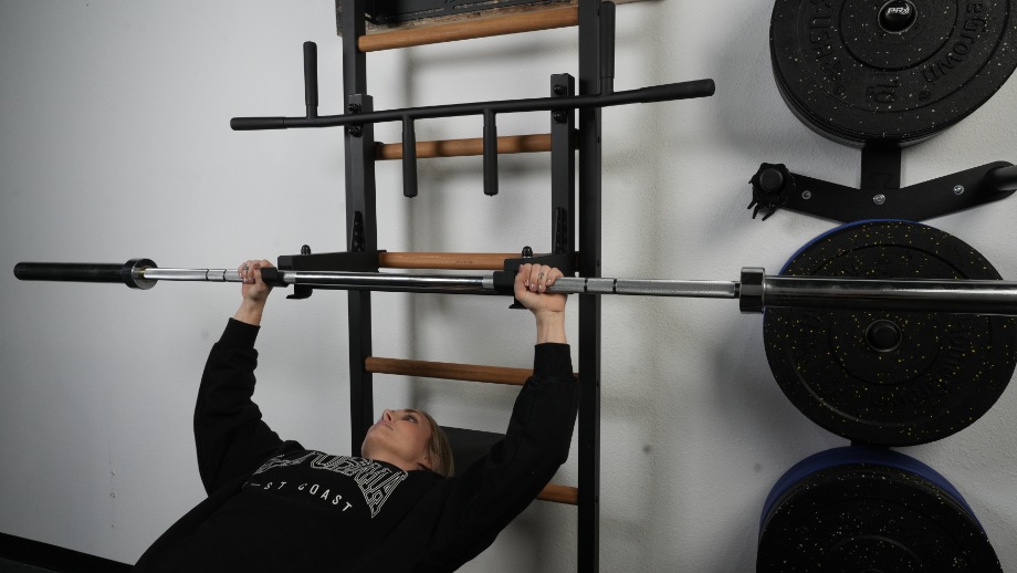 A person doing bench presses on the BenchK Wall Bars.