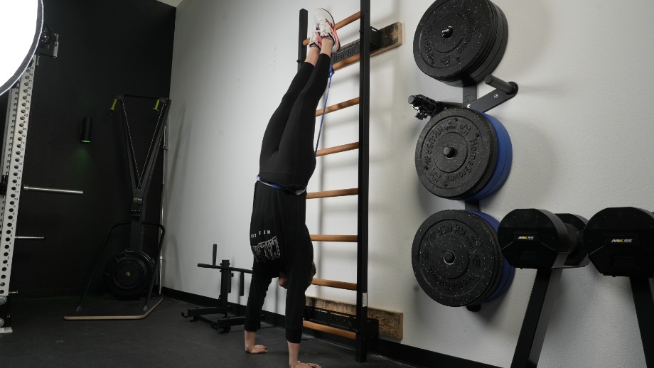 A person does a hand stand against the BenchK Wall Bars.