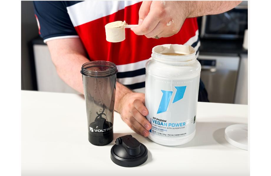 caine scooping 1st Phorm Vegan Power pro from a white container into a black shaker cup 