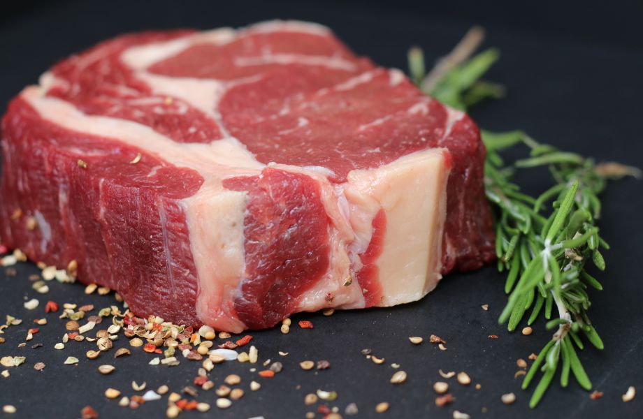 A thickly-sliced raw steak beside a sprig of fresh rosemary