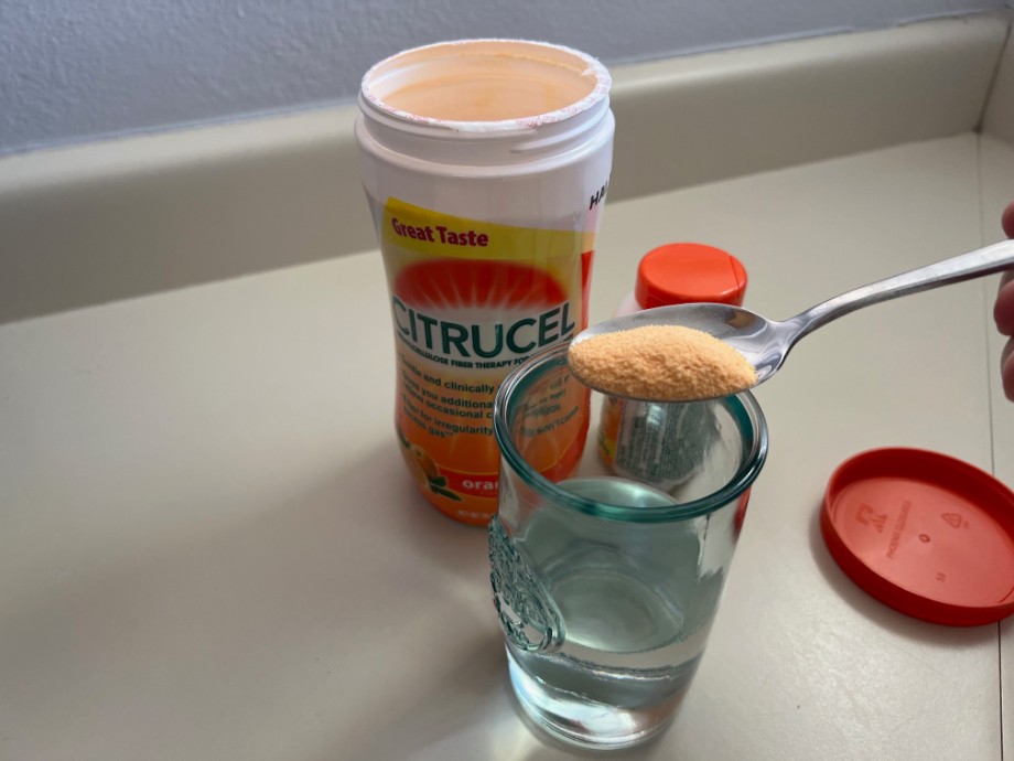 A person holds a scoop of Citrucel over a glass of water