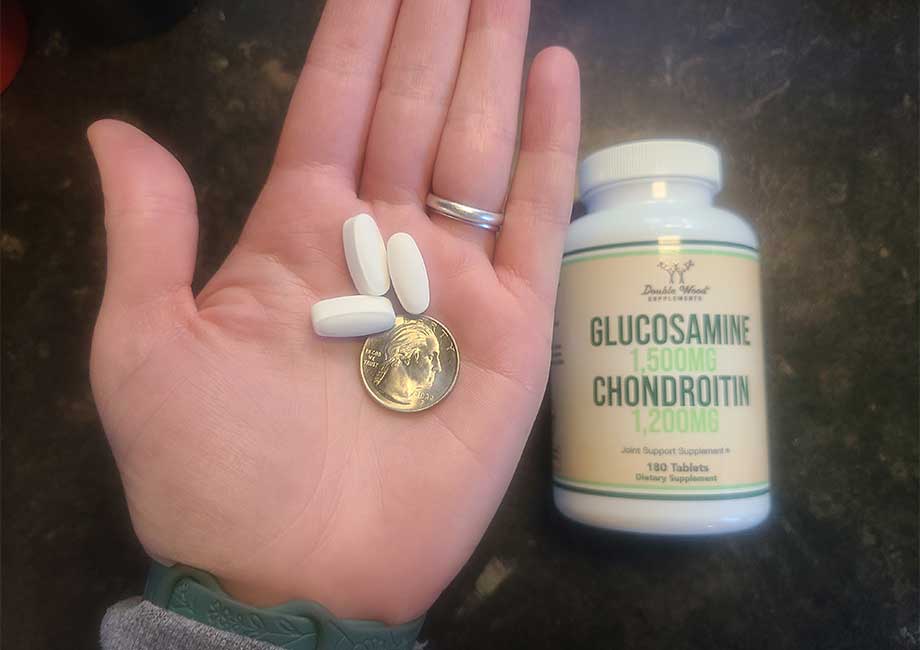 A person holds a few Double Wood Glucosamine Chondroitin Joint Supplement capsules with a quarter for size comparison.