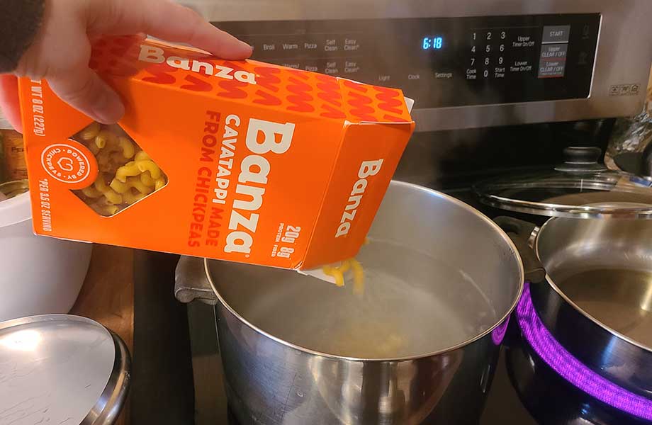 Dumping Banza protein pasta into a pot.