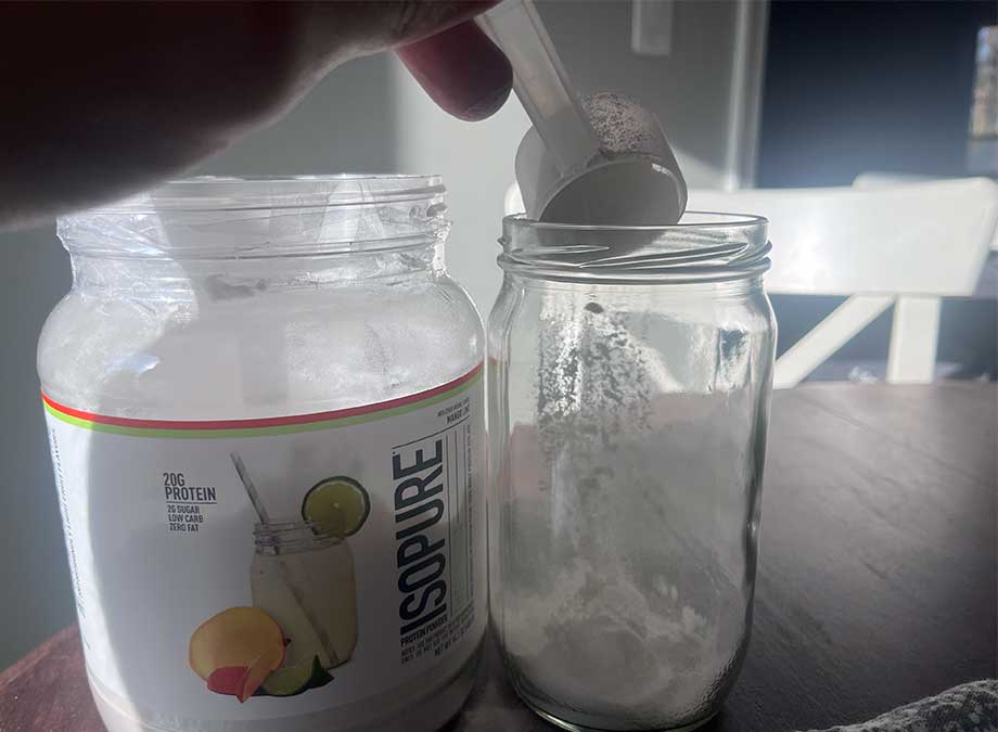 A scoop of Isopure Infusions Protein Powder is poured into a glass.