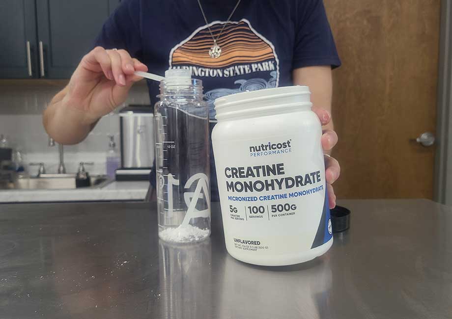 Someone dumping a scoop of Nutricost Creatine into a shaker