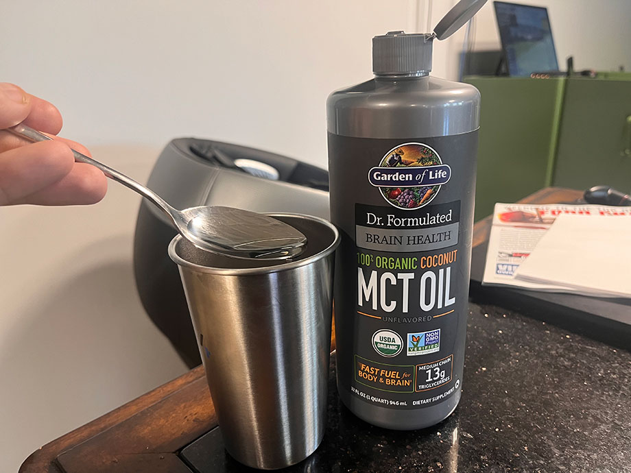 A spoon of Garden of Life Coconut MCT Oil held next to the container