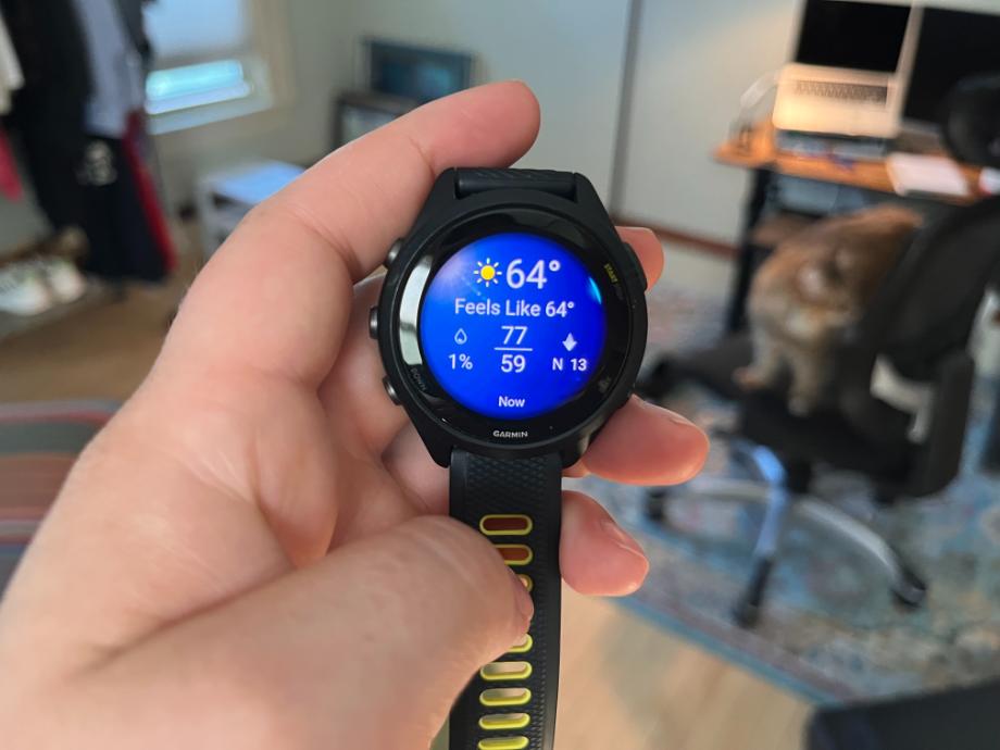 A woman holds up a Garmin Forerunner 265 to display the watch face.