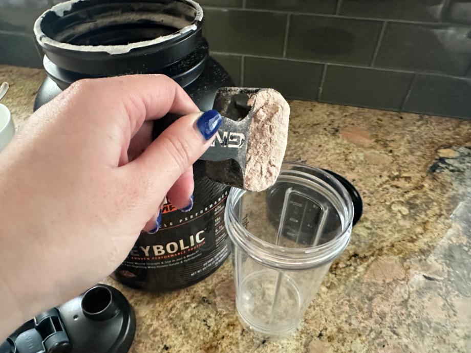 Scooping some GNC AMP Wheybolic Protein Powder into a shaker glass.