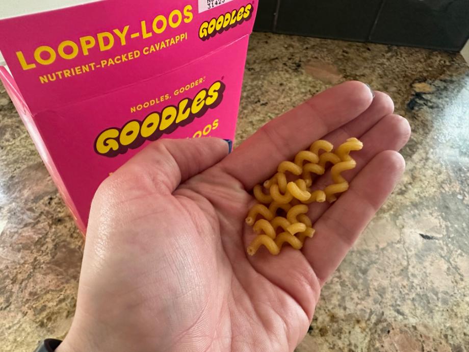 A hand holds some uncooked Goodles pasta.
