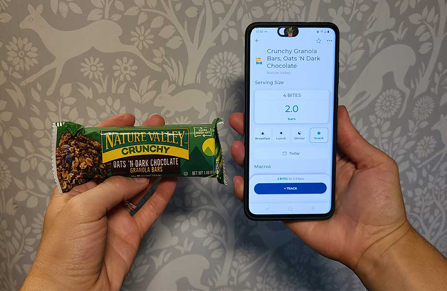 A person holds a granola bar up next to a phone with the Heathi food tracking app.