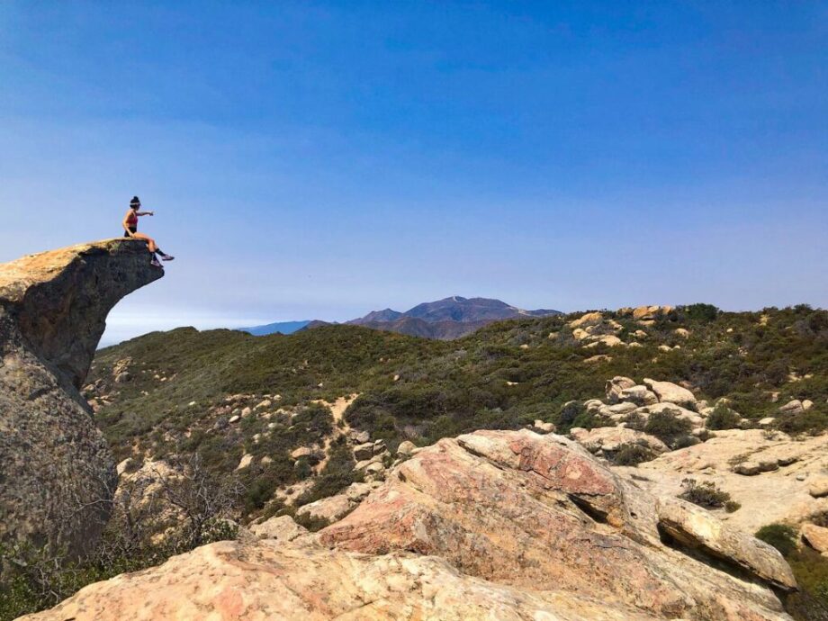 A woman sitting on top of a hiking summit pointing into the distance - outdoor training guide