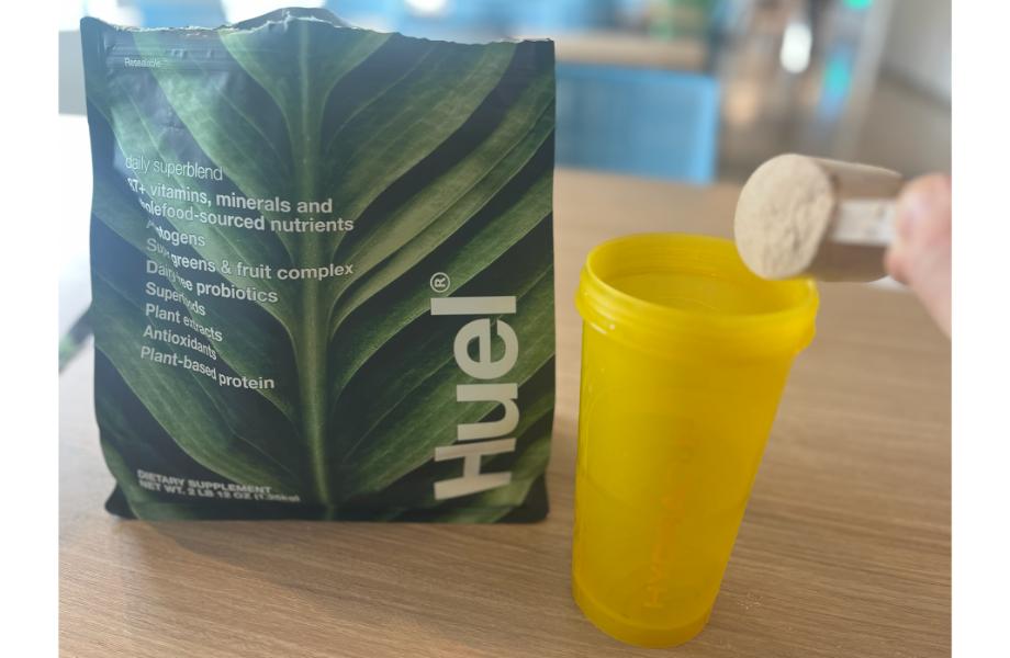 Huel daily superblend being scooped into a yellow shaker cup 