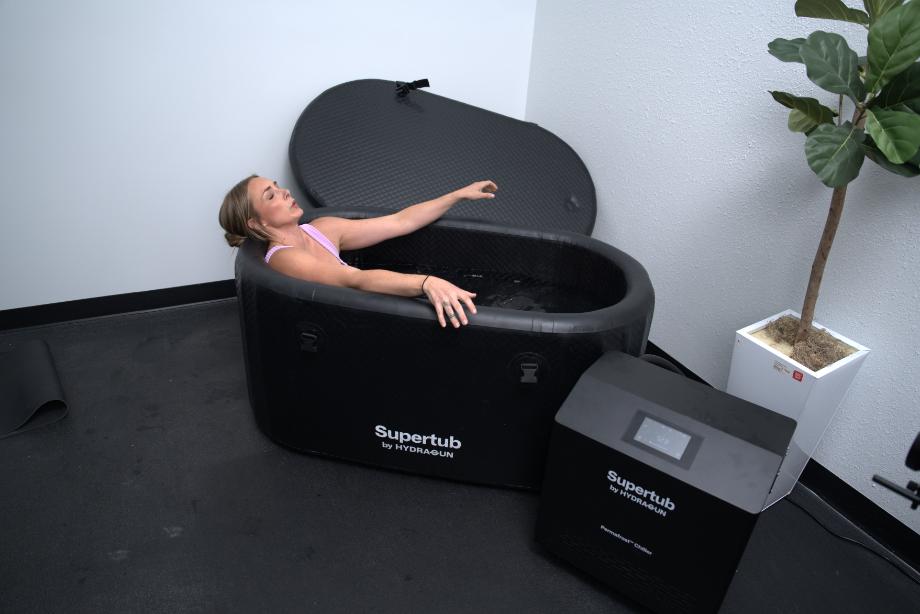 A woman sits in a Hydragun Supertub Cold Plunge while leaning her head back on the edge of the tub.