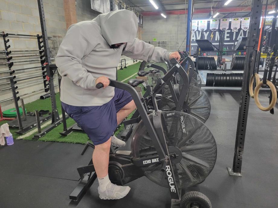 Man biking on an exercise bike while wearing the Kutting Weight Hoodie V4