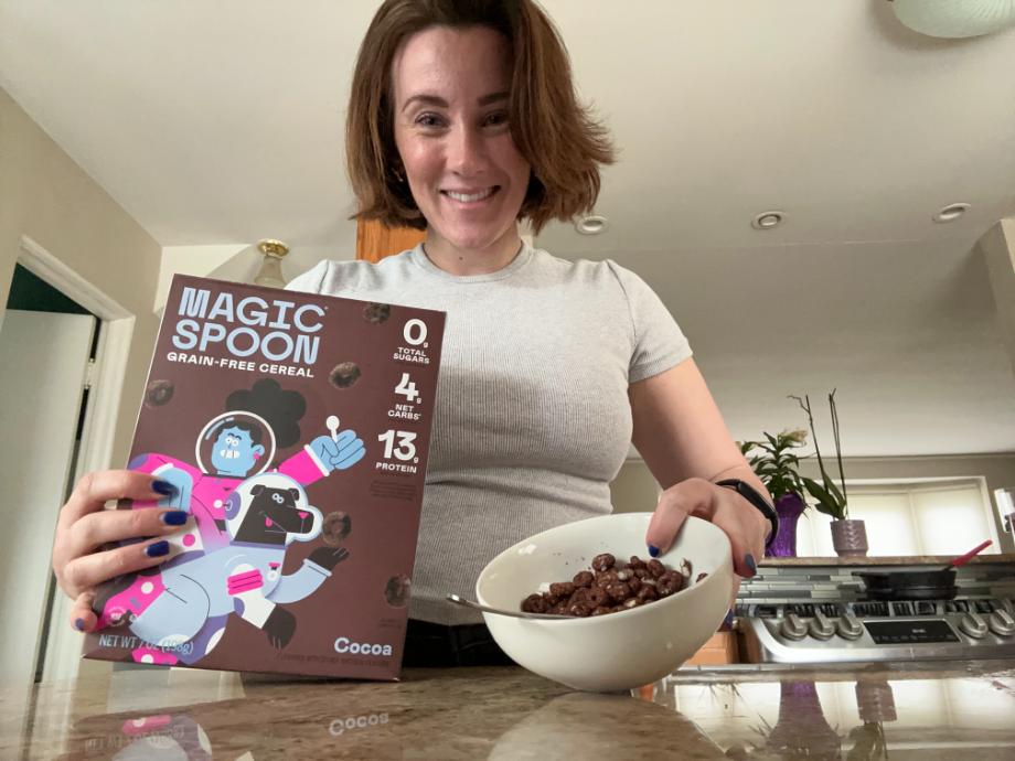 A woman holds a box of Magic Spoon Protein Cereal.