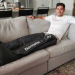 A person lounges on a couch with Normatec Elite Recovery Legs.