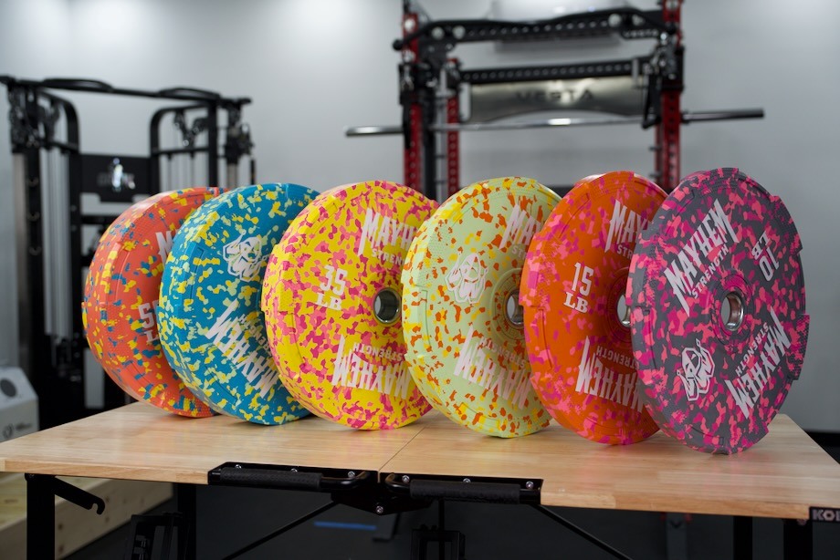 A set of Mayhem Strength Bumper Plates, stood up in a row like dominoes.