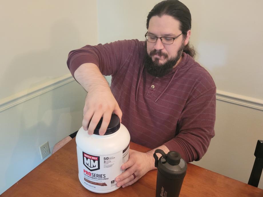 Man opening container of Muscle Milk Pro Series protein powder