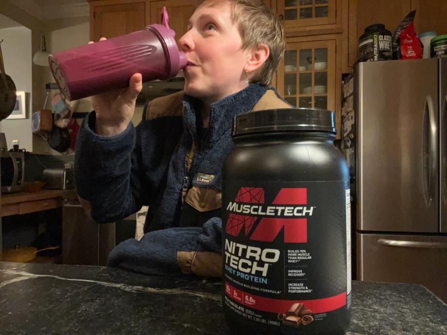 A woman drinks MuscleTech Nitro Tech from a shaker.