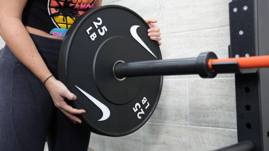 Woman loading a Nike barbell with a Nike bumper plate