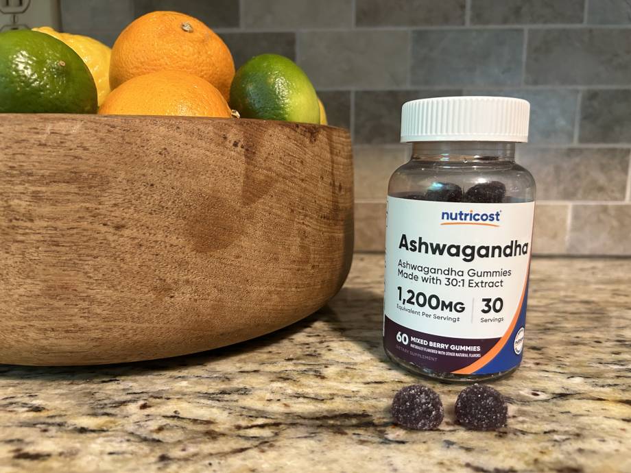 Some Nutricost Ashwagandha Gummies rest on a counter next to the bottle.
