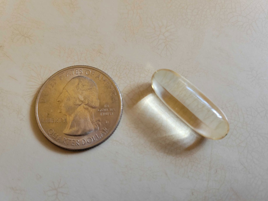 A Nutricost MCT Oil capsule next to a quarter for size comparison