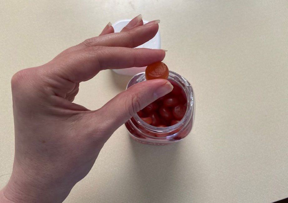 A hand holds up a single gummy from a bottle of Olly Undeniable Beauty