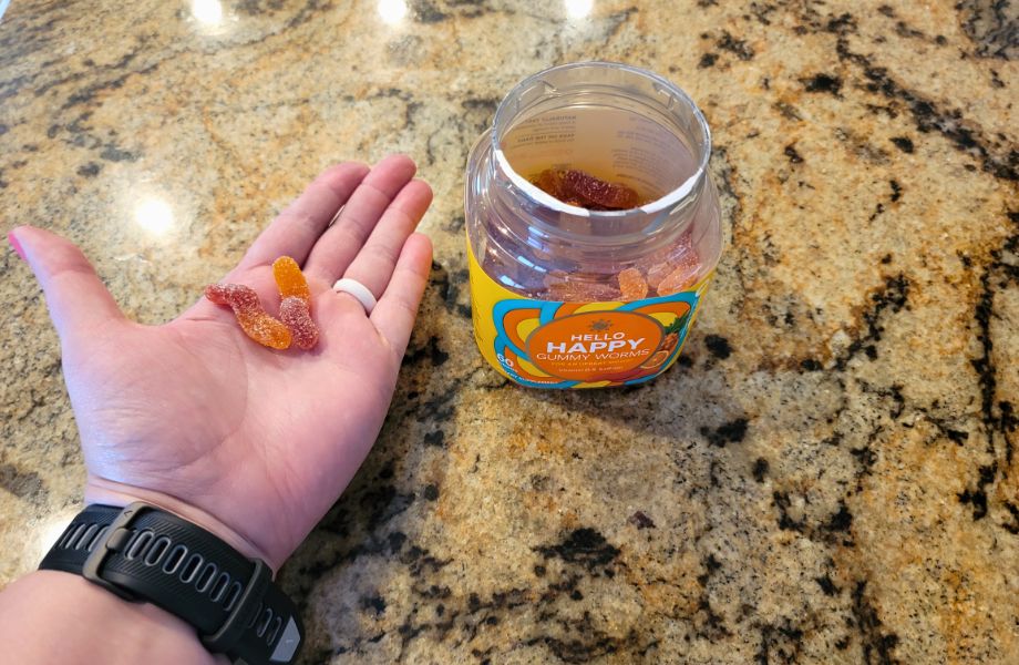 A hand holding some Olly Hello Happy gummy worms next to the opened jar.