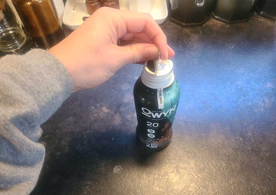 A hand removing the metal seal on an OWYN Protein shake bottle