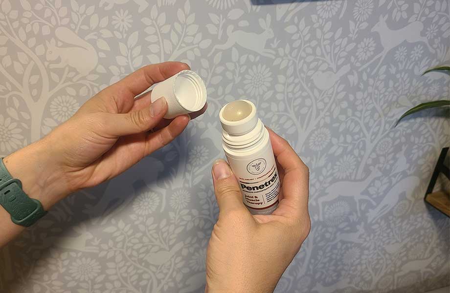 A person pops the cap off of a Penetrex Pain Cream roll-on applicator bottle.