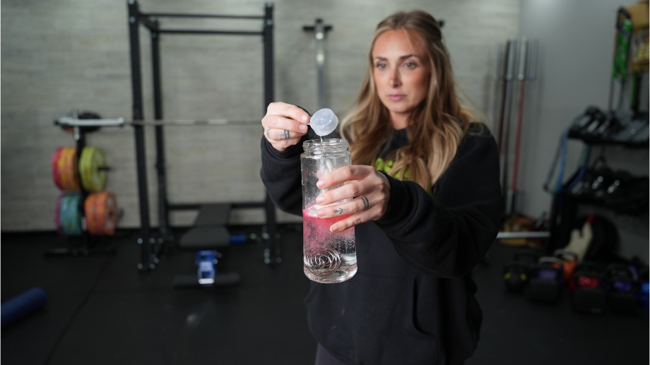 woman pouring Optimum Nutrition Gold Standard Pre-Workout into a clear shaker bottle. The water is turning red from the powder. 