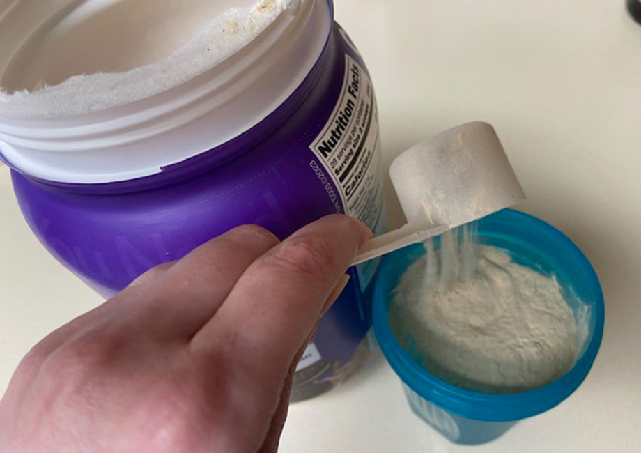A scoop of OWYN Plant Protein Powder is being poured into a shaker cup.