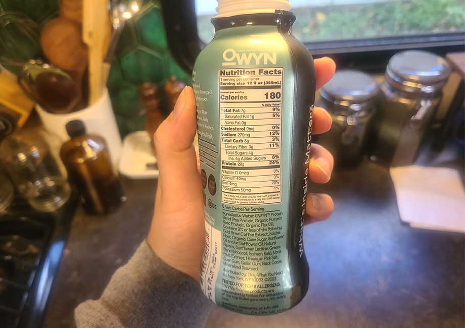 Someone holding an OWYN protein shake bottle so you can see the nutrition label 