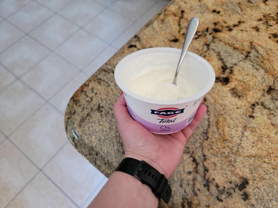 A hand holding a container of FAGE 0% Greek yogurt