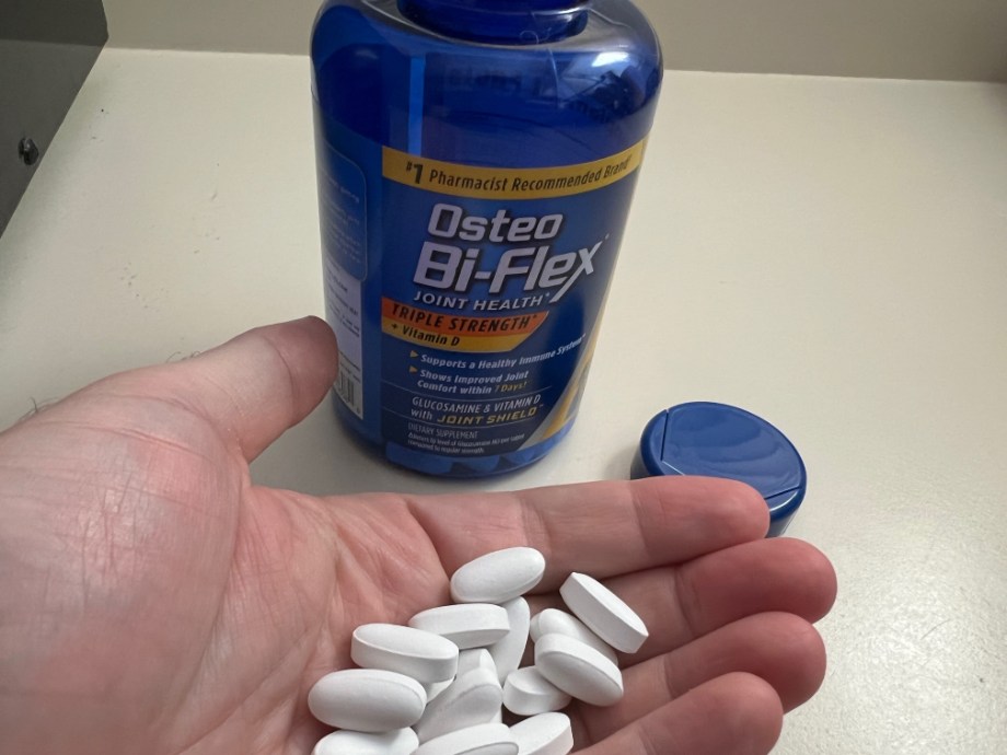 A person holds a handful of Osteo Bi-Flex capsules next to the opened bottle