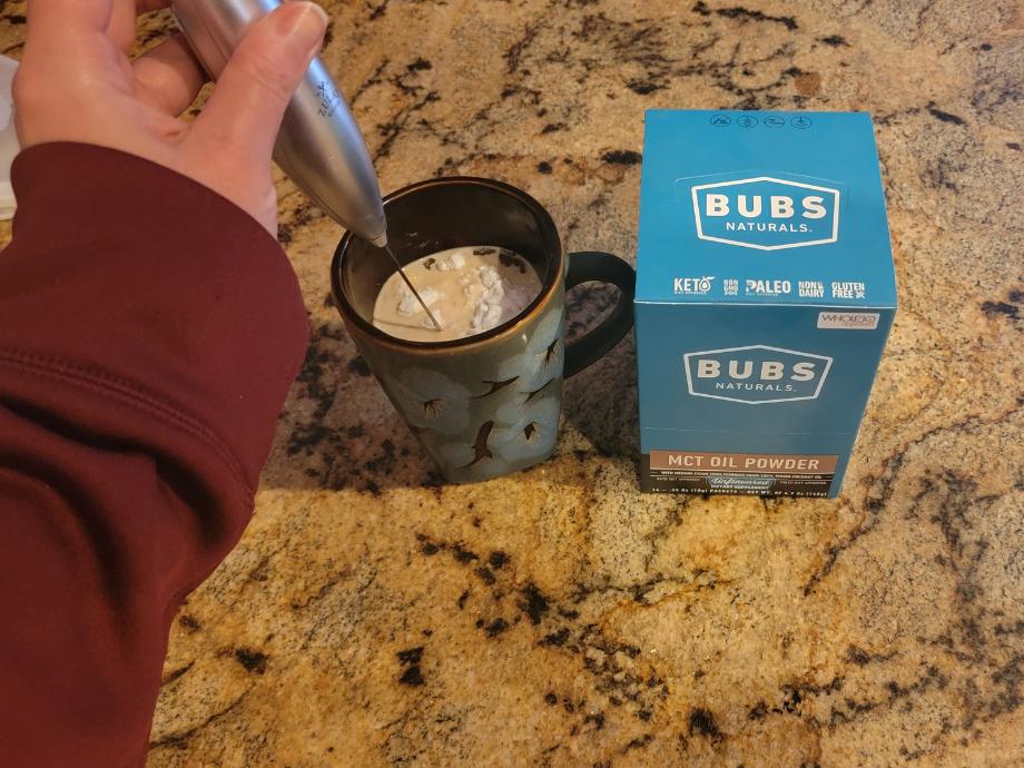 A person mixing BUBS MCT Oil powder in a cup of coffee with the frother