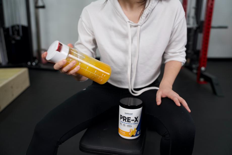 Person on a weight bench shaking a bottle of Nutricost Pre-X