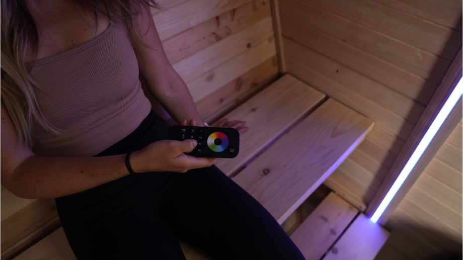 Our tester sits on the bench inside a Plunge Sauna, holding the LED remote.