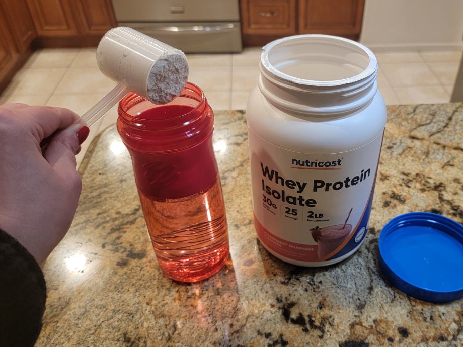 Person pouring Nutricost Whey Protein Isolate in the Strawberry flavor into a water bottle