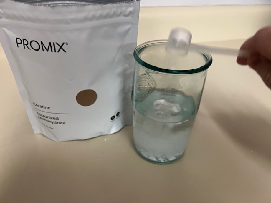 Person pouring a scoop of Promix Creatine into a glass of water