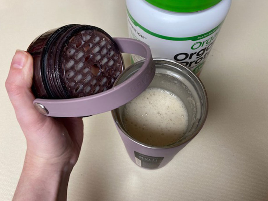 A person holding the lid and agitator of the Brumate Multishaker Bottle, showing the freshly mixed protein shake