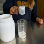 woman scooping protein powder into a mason jar