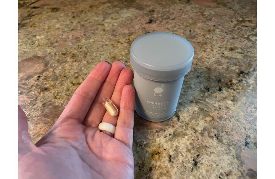 A hand holding Ritual Synbiotic pills next to the bottle.
