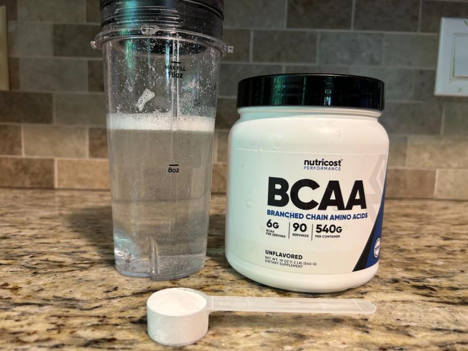 A scoop of Nutricost BCAA Powder rests in front of the container and a freshly mixed serving.