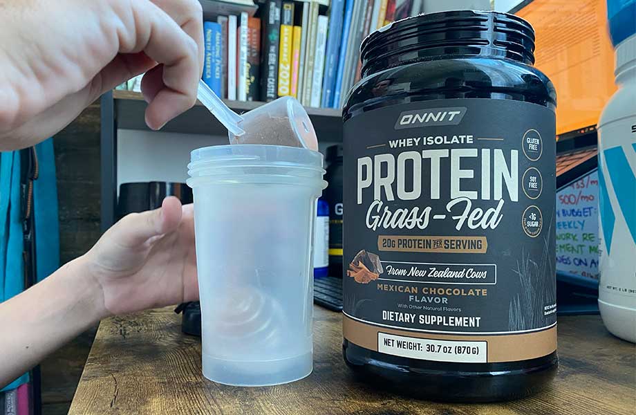A person scooping Onnit Grass-Fed Whey Isolate into a shaker cup.