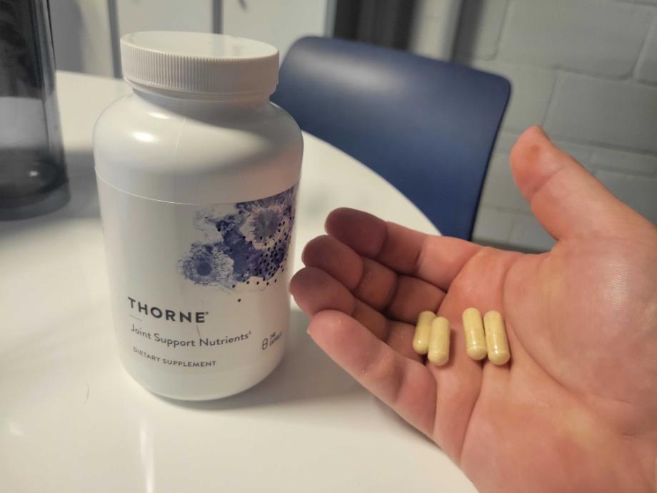 A person holds a few capsules of Thorne Joint Support next to the bottle.