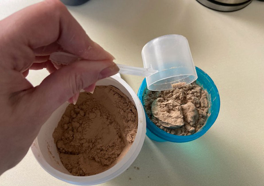 Dropping a scoop of Tone It Up Protein powder into a shaker cup.